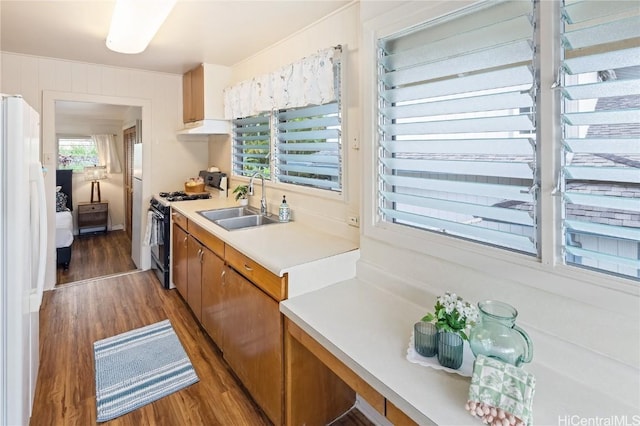 kitchen with brown cabinetry, dark wood-style floors, light countertops, a sink, and gas stove