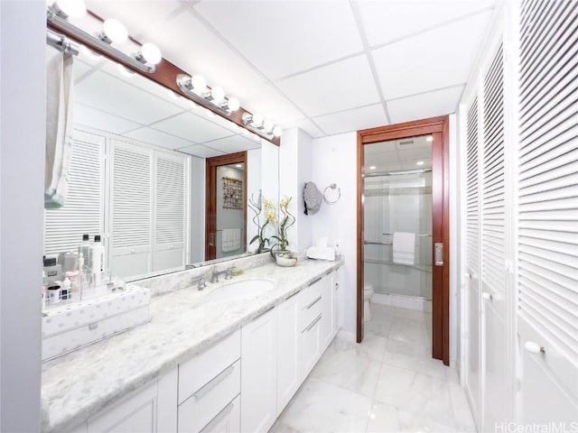 bathroom with a shower with door, vanity, a drop ceiling, and toilet