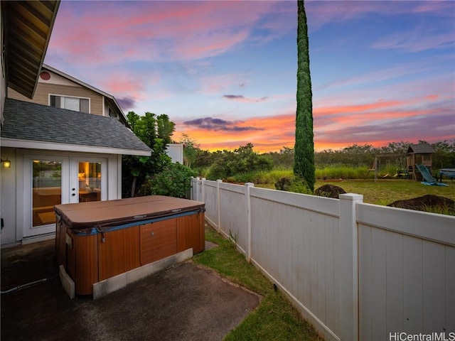 patio terrace at dusk with french doors, a hot tub, and a playground