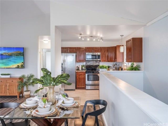 kitchen with lofted ceiling, tasteful backsplash, hanging light fixtures, light wood-type flooring, and stainless steel appliances