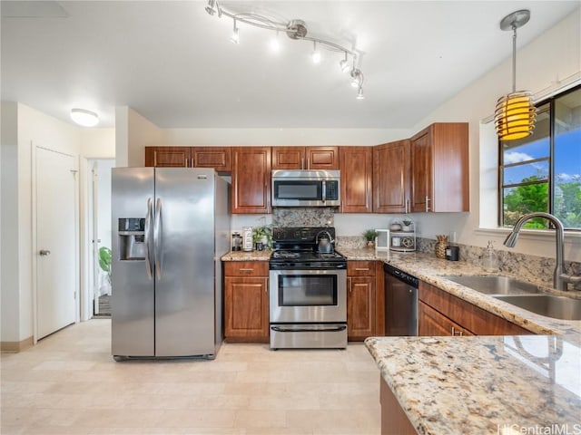 kitchen with appliances with stainless steel finishes, sink, light stone counters, and decorative light fixtures