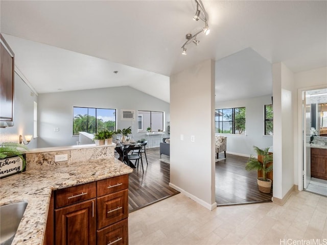 kitchen with track lighting, lofted ceiling, light stone countertops, and light wood-type flooring