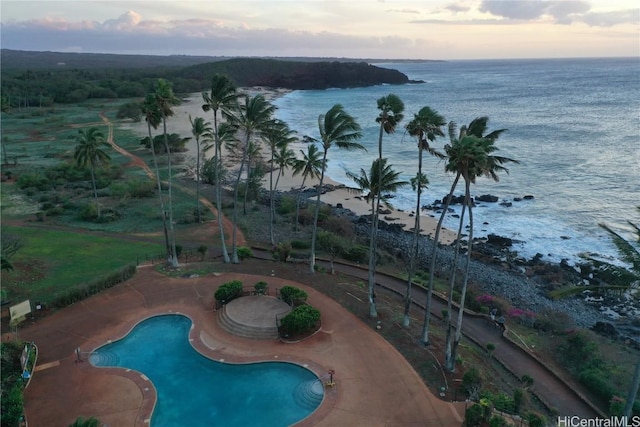 pool at dusk featuring a water view and a patio area