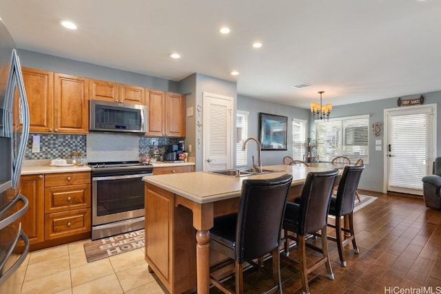 kitchen featuring sink, tasteful backsplash, decorative light fixtures, an island with sink, and stainless steel appliances