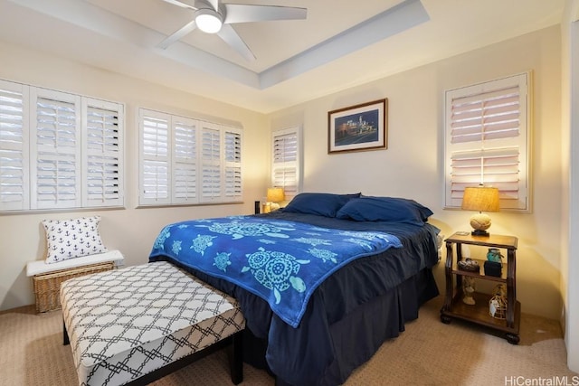 bedroom featuring a tray ceiling, light colored carpet, and ceiling fan