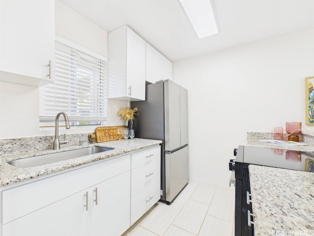 kitchen with a sink, light stone countertops, freestanding refrigerator, and white cabinetry