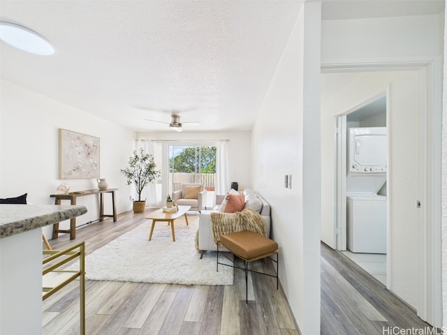 living room featuring a ceiling fan, wood finished floors, stacked washer and clothes dryer, and a textured ceiling