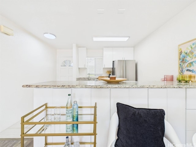 kitchen with light stone countertops, a peninsula, freestanding refrigerator, a sink, and white cabinetry