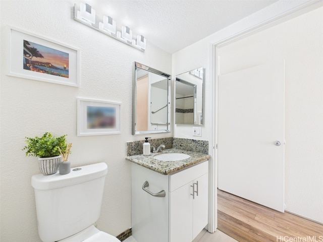 bathroom featuring toilet, wood finished floors, vanity, and a textured ceiling