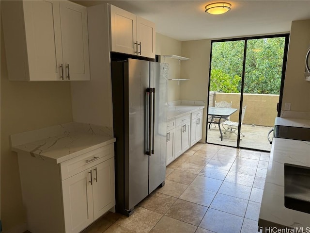 kitchen with light tile patterned flooring, high quality fridge, white cabinets, light stone counters, and floor to ceiling windows