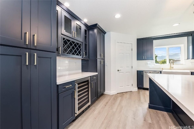 kitchen featuring tasteful backsplash, dishwasher, sink, beverage cooler, and light wood-type flooring