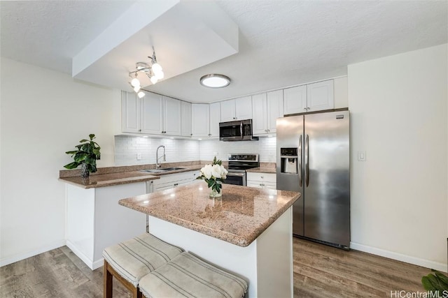 kitchen featuring sink, kitchen peninsula, white cabinets, stainless steel appliances, and backsplash