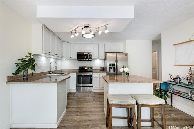 kitchen featuring sink, a breakfast bar area, white cabinets, kitchen peninsula, and stainless steel appliances