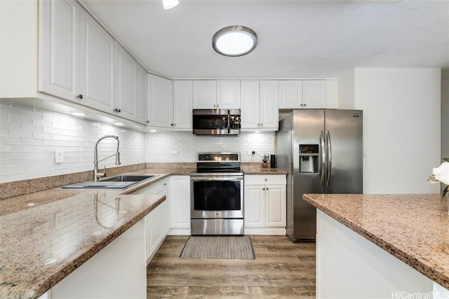 kitchen with sink, stainless steel appliances, white cabinets, and light stone countertops