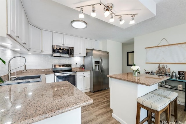 kitchen featuring sink, light hardwood / wood-style flooring, stainless steel appliances, light stone counters, and white cabinets