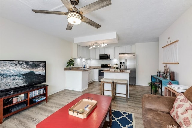 living room with ceiling fan with notable chandelier, sink, and light hardwood / wood-style flooring