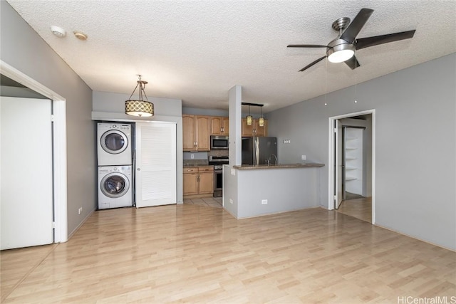 kitchen featuring appliances with stainless steel finishes, decorative light fixtures, stacked washer and dryer, light hardwood / wood-style floors, and a textured ceiling