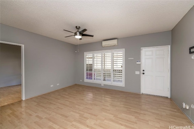 interior space featuring a wall mounted air conditioner, a textured ceiling, ceiling fan, and light hardwood / wood-style floors