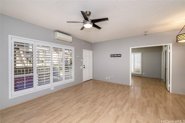 unfurnished room with ceiling fan, a wall mounted AC, light hardwood / wood-style flooring, and a textured ceiling