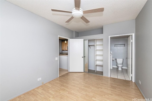 unfurnished bedroom with ceiling fan, ensuite bathroom, a textured ceiling, a closet, and light wood-type flooring