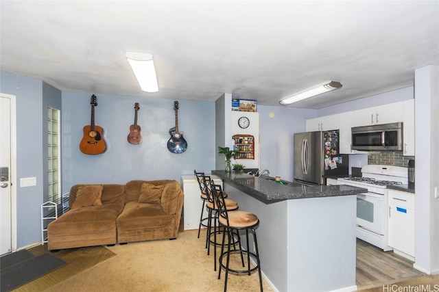 kitchen with a breakfast bar, appliances with stainless steel finishes, white cabinetry, backsplash, and kitchen peninsula