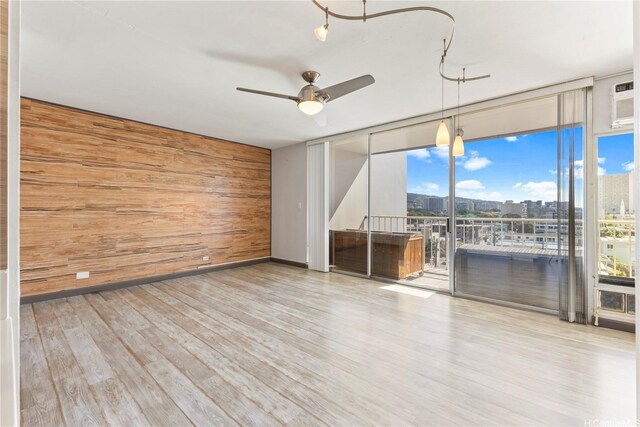 spare room with wooden walls, a ceiling fan, expansive windows, wood finished floors, and healthy amount of natural light