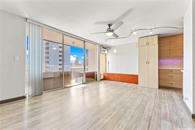unfurnished room with floor to ceiling windows, light wood-style flooring, ceiling fan, a wall unit AC, and a view of city