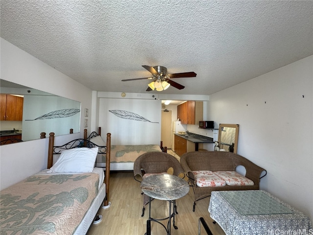 bedroom with light wood-type flooring, a textured ceiling, and a ceiling fan