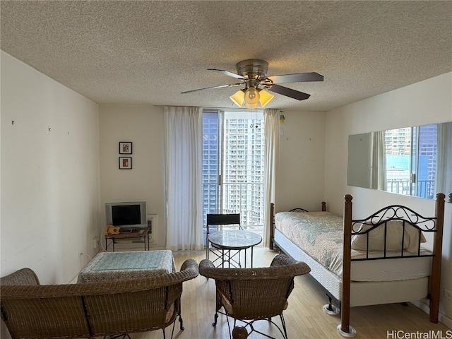 bedroom featuring a ceiling fan, light wood-style flooring, floor to ceiling windows, and a textured ceiling