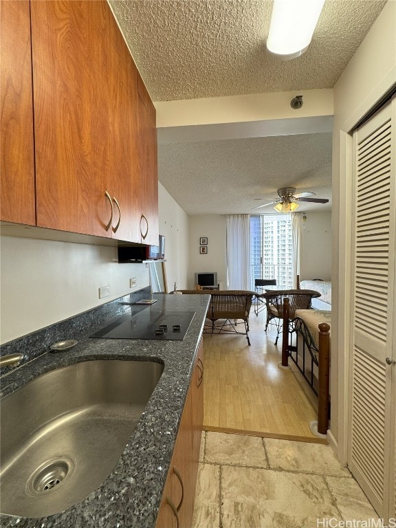 kitchen featuring ceiling fan, black electric stovetop, brown cabinets, and a sink