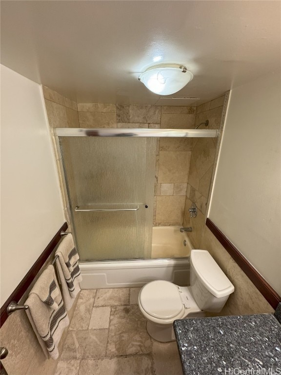 full bathroom featuring enclosed tub / shower combo, toilet, and stone tile floors