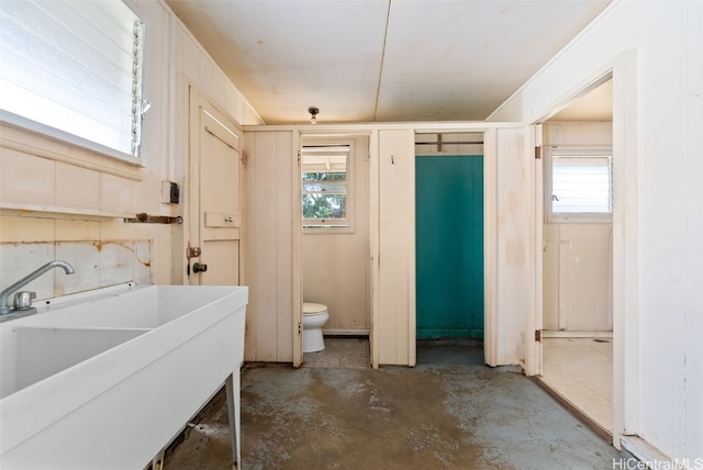 bathroom with sink, toilet, concrete floors, and a healthy amount of sunlight