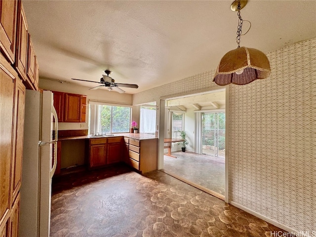 kitchen with hanging light fixtures, a textured ceiling, kitchen peninsula, white fridge, and ceiling fan