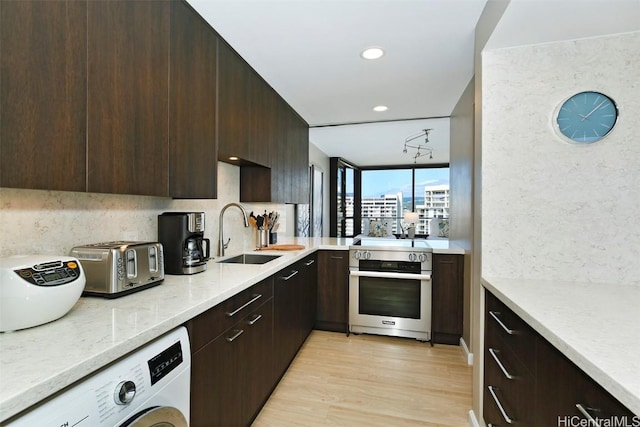 kitchen featuring washer / dryer, sink, light stone counters, light wood-type flooring, and high end stainless steel range oven