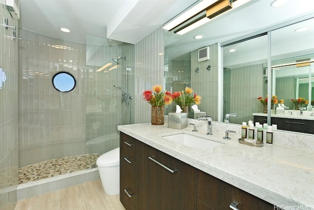 bathroom with hardwood / wood-style flooring, tiled shower, vanity, and toilet