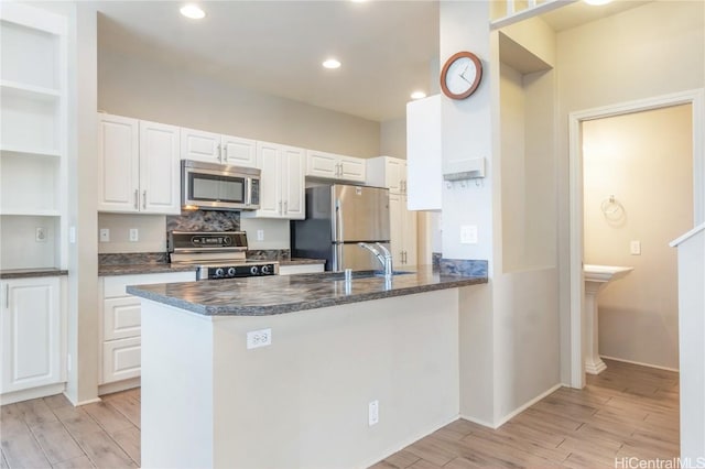 kitchen featuring appliances with stainless steel finishes, white cabinets, light wood-type flooring, and kitchen peninsula