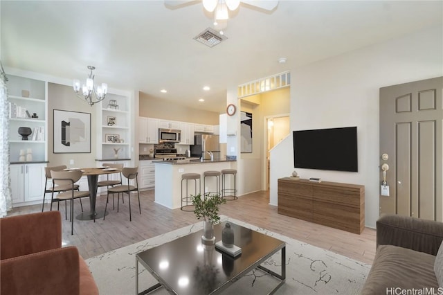 living room with ceiling fan with notable chandelier, built in features, and light hardwood / wood-style flooring