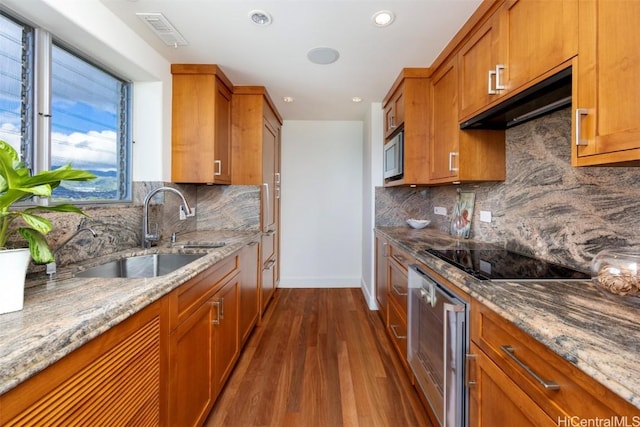 kitchen with range hood, sink, dark hardwood / wood-style flooring, light stone countertops, and black electric cooktop