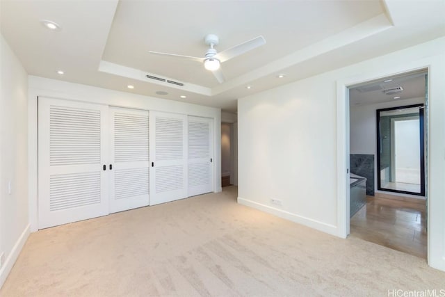 unfurnished bedroom with a raised ceiling, light colored carpet, and a closet