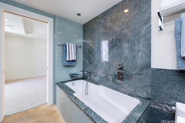 bathroom with toilet, tile patterned flooring, tile walls, and tiled tub