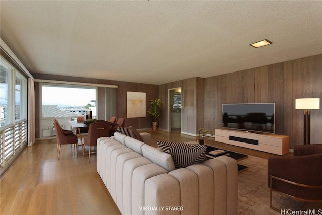 living room featuring light hardwood / wood-style flooring, wooden walls, and a textured ceiling