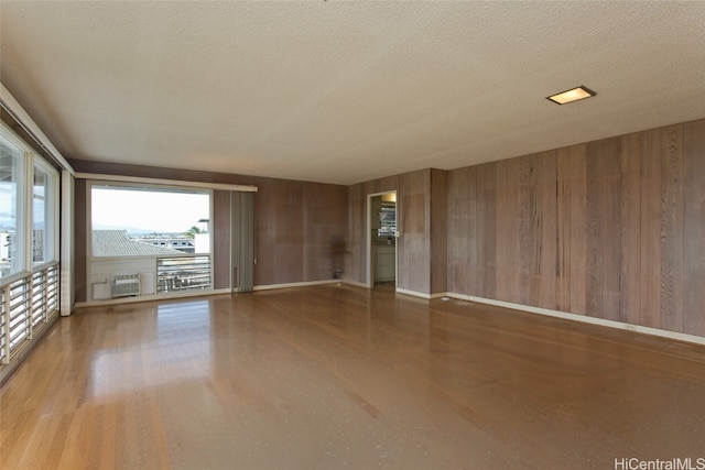 empty room with wooden walls, a wall unit AC, and a textured ceiling