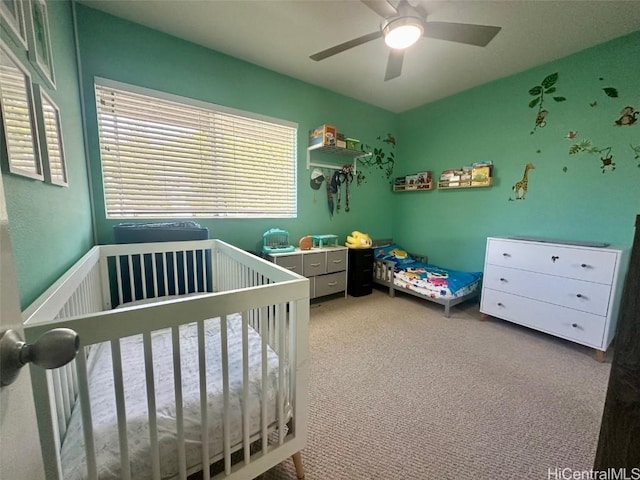 carpeted bedroom with a crib and ceiling fan