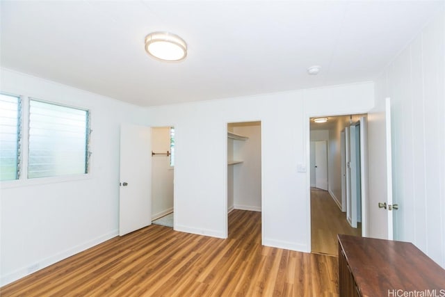 unfurnished bedroom featuring multiple windows, wood-type flooring, a spacious closet, and a closet