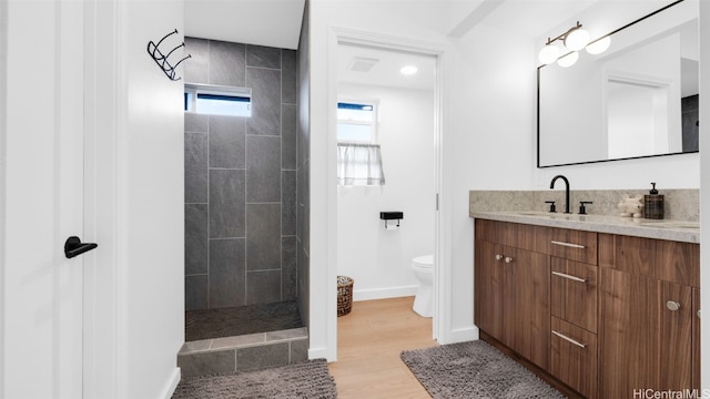 bathroom with hardwood / wood-style flooring, vanity, a tile shower, and toilet