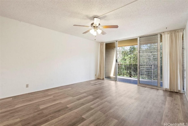 spare room with a textured ceiling, wood finished floors, a ceiling fan, and expansive windows