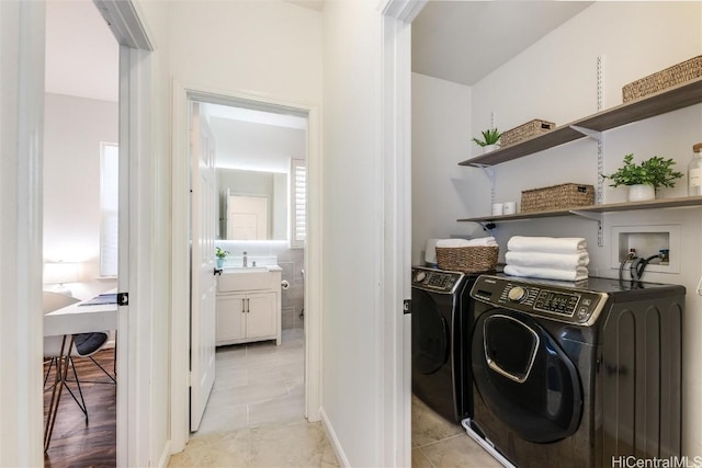 clothes washing area featuring sink, light tile patterned floors, and washer and clothes dryer