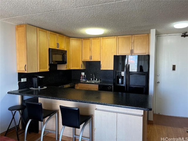 kitchen with black appliances, wood-type flooring, sink, a kitchen bar, and kitchen peninsula