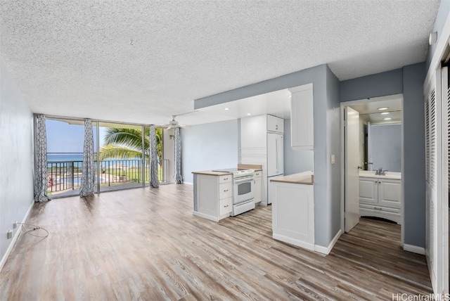 kitchen with white electric stove, sink, white cabinets, floor to ceiling windows, and light wood-type flooring