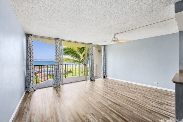 unfurnished room with a water view, wood-type flooring, a textured ceiling, ceiling fan, and a wall of windows